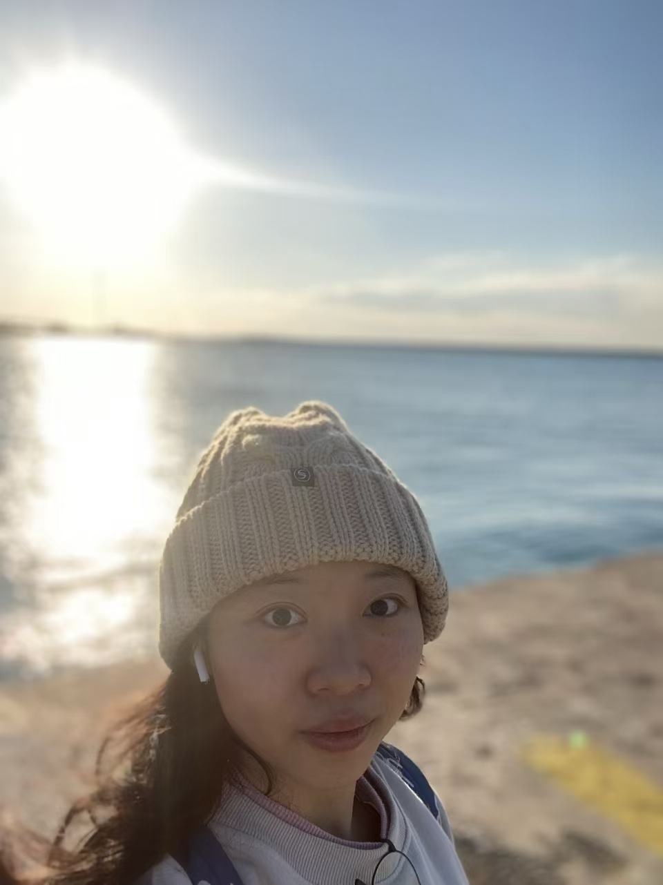 Rui by the sea in soft sunlight, wearing a knitted hat.