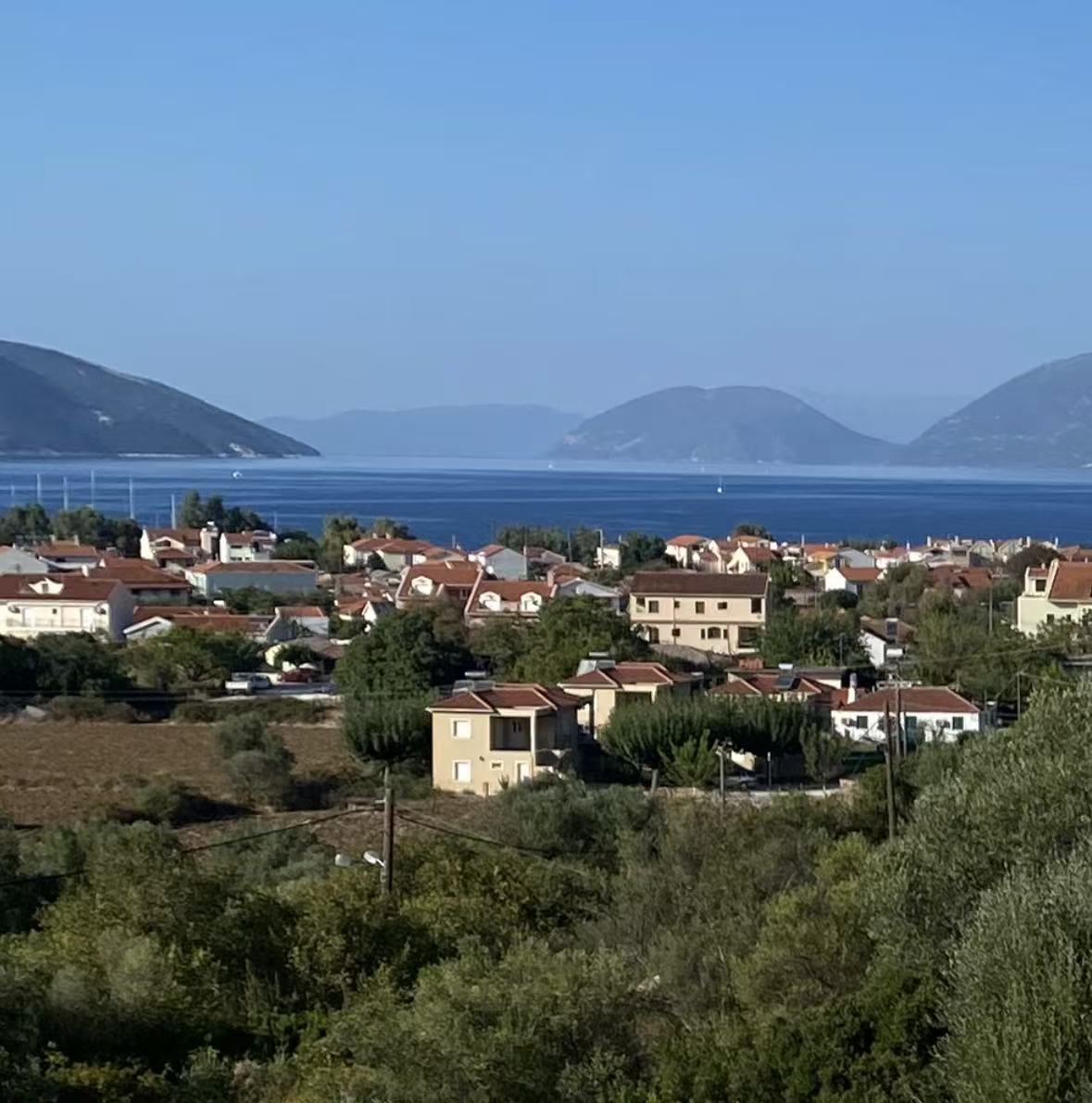 Rui’s view across Sami, Kefalonia: red-roofed houses, blue water and distant island hills.